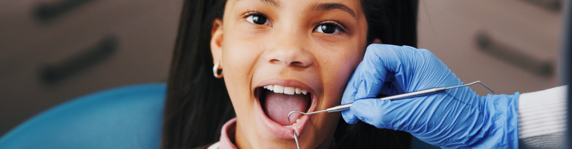 Gloved hands using dental tools in girl's mouth.